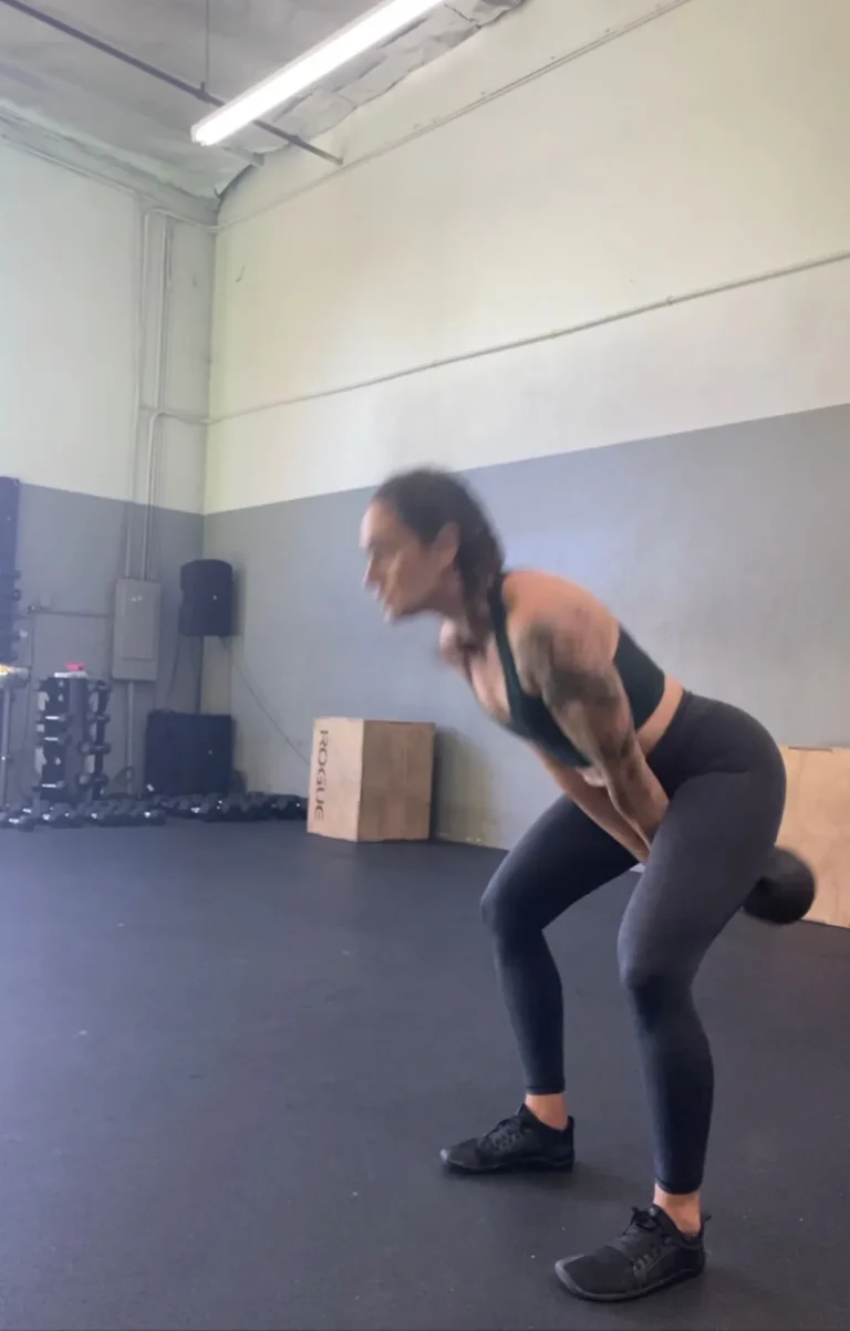 A woman performing a kettlebell swing movement in a gym.