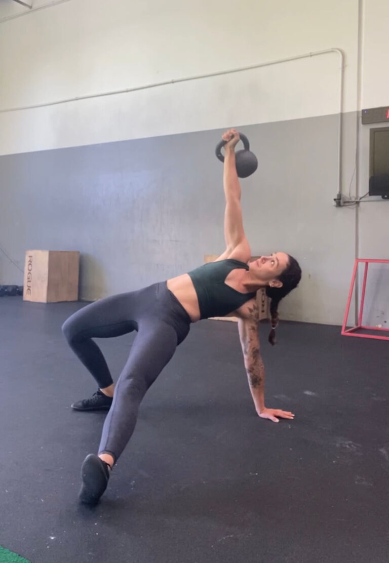 A woman performing a Turkish get-up exercise with a kettlebell.