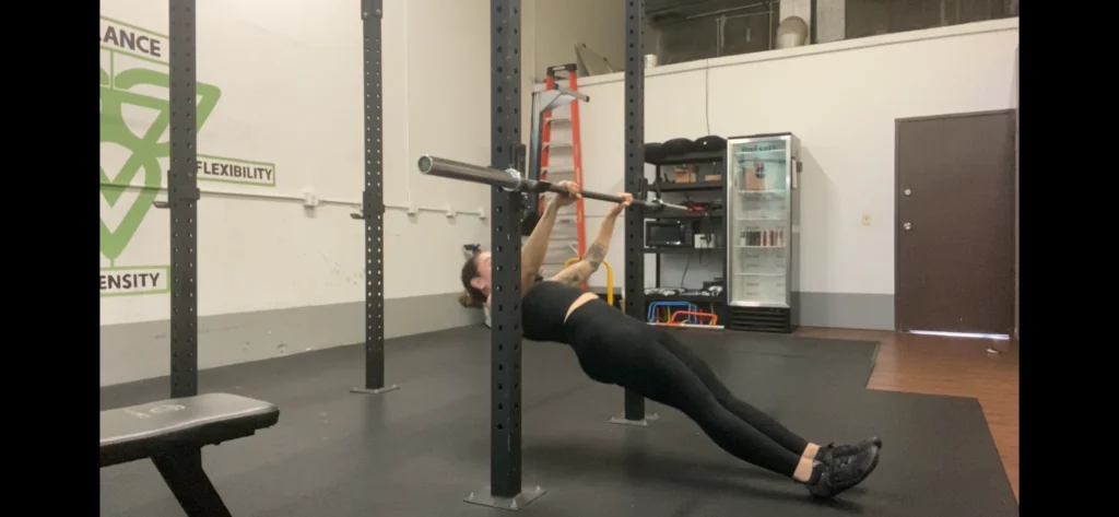 A woman demonstrating how to perform the Australian pull-up on a low chin-up bar